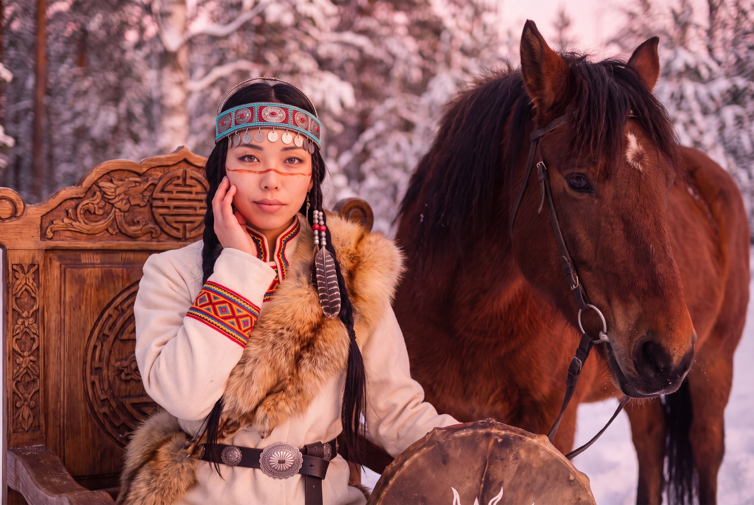 UYANA beside her bay horse in a snowy forest, sitting by a carved wooden throne with her drum